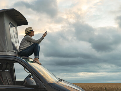 woman sitting on top of car searching for service on her cellphone