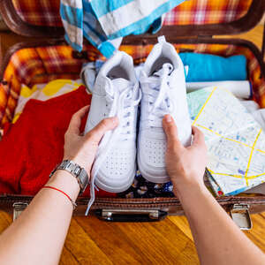 A person's hands putting sneakers into a suitcase. 