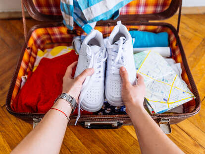 A person's hands putting sneakers into a suitcase. 