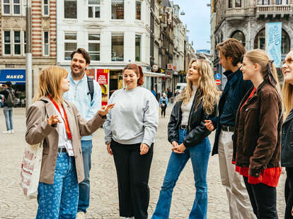 A group of young people standing around a tour guide in a European city. 