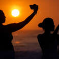 People use their mobile phones to take photos on the beach as the sun sets.