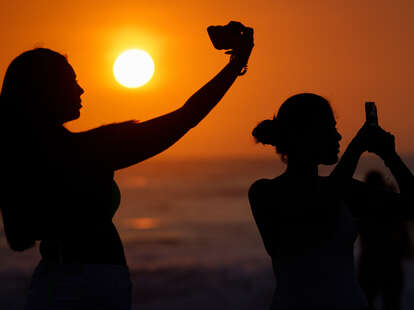 People use their mobile phones to take photos on the beach as the sun sets.