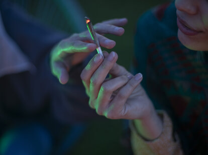 A close-up shot of two people passing a joint of marijuana