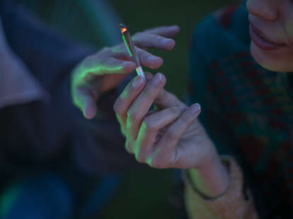 A close-up shot of two people passing a joint of marijuana