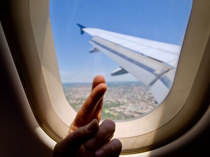 a hand with fingers crossed in front of an airplane window
