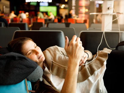 Woman lying and using a smartphone charging port at airport.