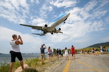 people with cell phones looking up and taking pictures of a plane in greece