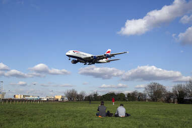 people sit on grass watching a massive Airbus A380 arrive in London