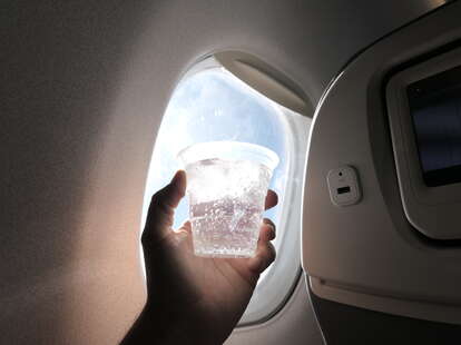 Hand holds a glass in front of the plane window.
