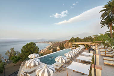 a cliffside pool with umbrellas with a volcano in the background 