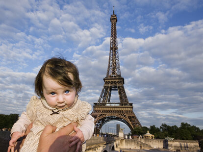 A baby being held aloft in front of the Eiffel Tower, Paris, France.