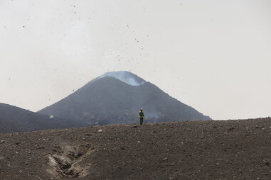 a man standing in front of a volcano spewing rocks and ash