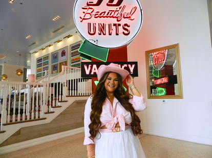 A woman wearing a cowboy hat posing in front of a neon sign.