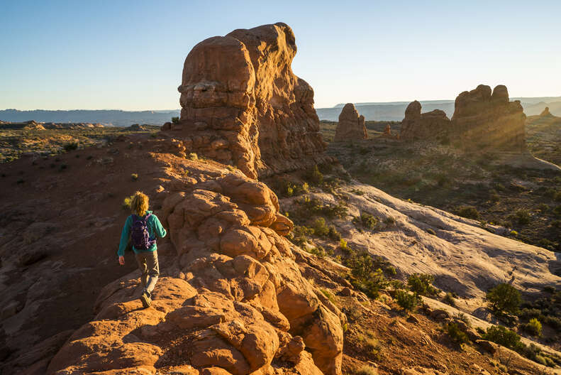 A woman hiking a scenic trail in the red rocks of Arches National Park.