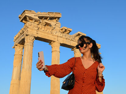 A woman takes a selfie by historical ruins in the temples area of the ancient city of Side during sunset in Manavgat district of Antalya, Turkiye on June 23, 2024.