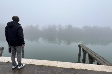 man looking out onto foggy venetian lagoon from dock