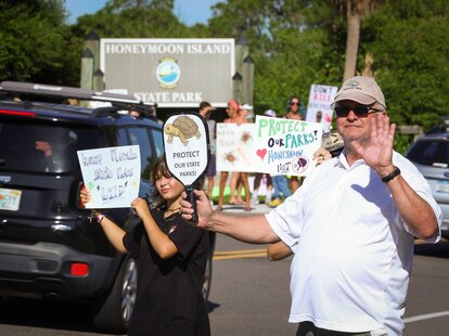 Ray Poynor, 61, of Odessa, right, holds a pickleball paddle along with Naomi Stracey, 14, left, of Tampa as drivers make their way into Honeymoon Island State Park during a rally Sunday, Aug. 25, 2024 in Dunedin, Florida.
