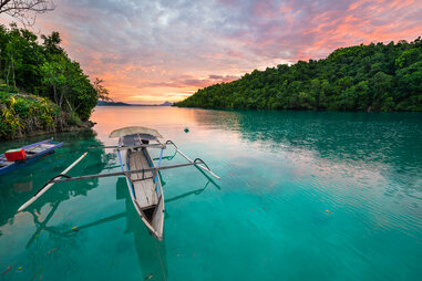 Breathtaking colorful sunset and traditional boat floating on scenic blue lagoon in the Togean (or Togian) Islands, Central Sulawesi, Indonesia,.
