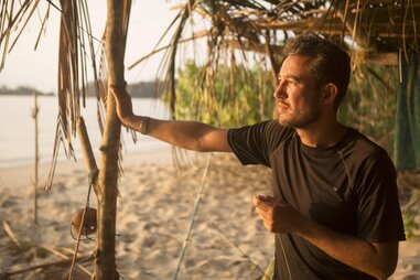 Tom Williams standing under a hut on a beach during the sunset.