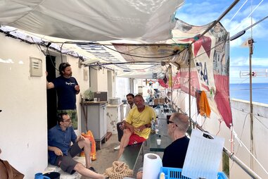 a group of men sitting on a patio, the sea in the background