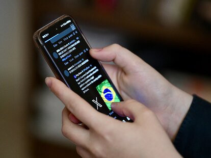 A Brazilian user of the social network X, formerly Twitter, browses posts on a cell phone in Brasilia on August 31, 2024.