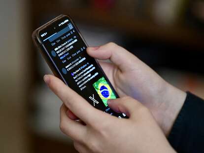 A Brazilian user of the social network X, formerly Twitter, browses posts on a cell phone in Brasilia on August 31, 2024.