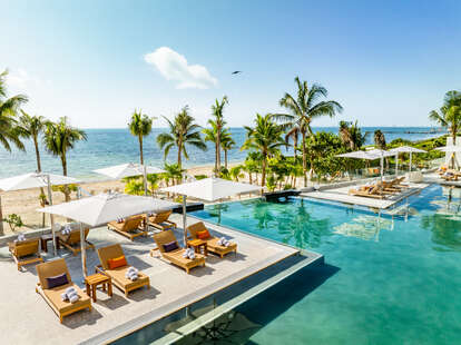 a shot of the beach from the pool of a resort, with coconut trees 