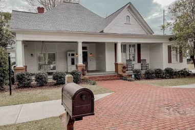 The exterior of a white colonial home that has a large front porch and brick walkway. It was Caroline Forbes' house in the Vampire Diaries.