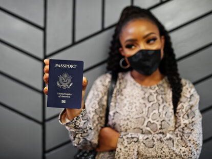 African american woman wearing black face mask show USA passport in hand.