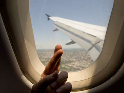 passenger crossing fingers while looking out an airplane window.