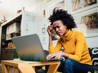 Woman looking stressed while working on her laptop at home.