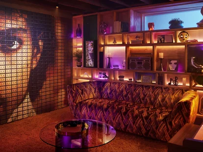 A living room in the Purple Rain house, featuring a leopard print sofa and a wall with Prince&rsquo;s face.