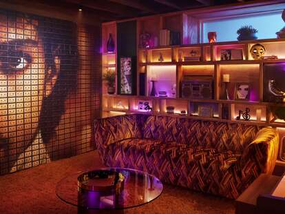 A living room in the Purple Rain house, featuring a leopard print sofa and a wall with Prince’s face.