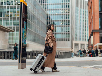 Young woman carrying luggage, walking on the high street in the city.