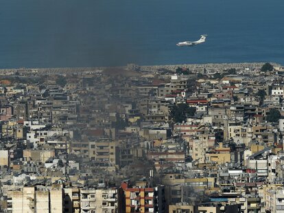 A plane flies over the city as smoke rises following an Israeli airstrike in Beirut, Lebanon on October 3, 2024.