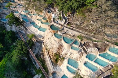people in natural hot springs lining the side of a lush mountain