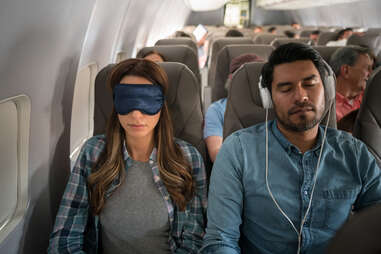 People traveling by air and sleeping on the plane wearing headphones and an eye mask.
