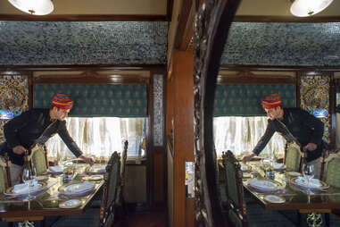 a man setting up dinner with opulent chairs and dining table on a train