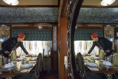 a man setting up dinner with opulent chairs and dining table on a train 