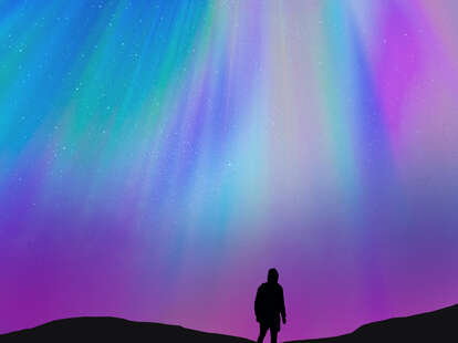 Silhouette of a guy with the beautiful colorful northern lights falling from the sky