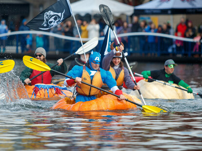 captain america, a bull, and other costumed adults using giant pumpkins as boats.