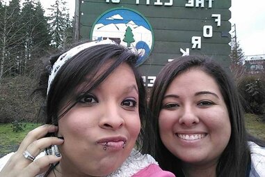 A photo showing two young women in front of the Welcome to Forks sign.