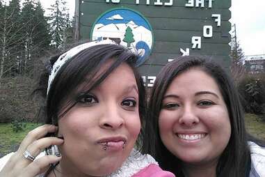 A photo showing two young women in front of the Welcome to Forks sign.