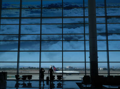 People stand beneath a picture of clouds on a large window as they watch planes take off from the Tom Bradley International terminal at Los Angeles International Airport (LAX) in Los Angeles, California, on August 10, 2022.