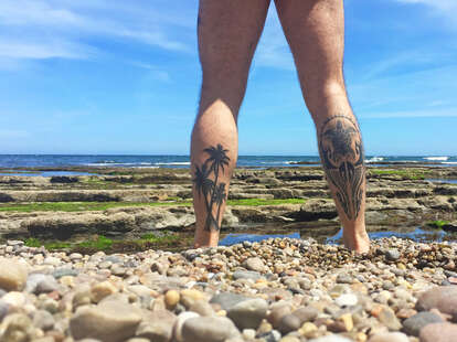 nude man with leg tattoos standing before the beach