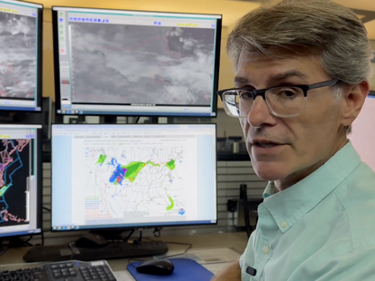 A meteorologist sitting at a desk explaining the weather for the FAA.