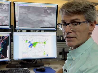 A meteorologist sitting at a desk explaining the weather for the FAA.