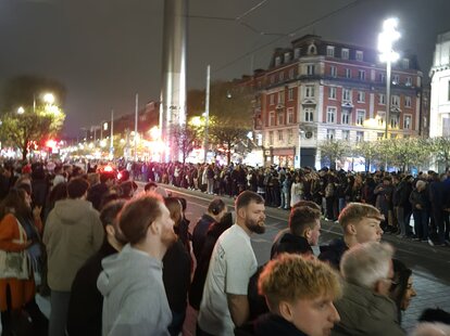 A photo of people waiting on an empty street for a parade that doesn’t exist.