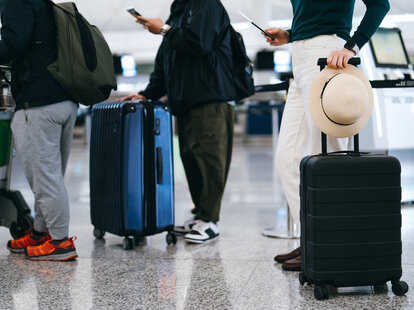 Cropped shot of group of airline passengers with suitcases standing in queue, waiting at check-in counter at International airport. Re