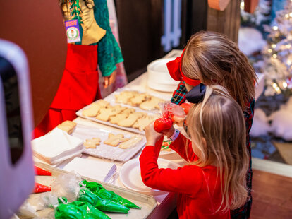 Three children run to their parents who are seated in a giant snow globe.